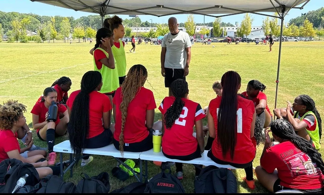 FitSquad girls’ soccer team meeting with their coach under a canopy
